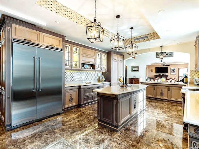 kitchen with decorative backsplash, a tray ceiling, pendant lighting, a center island, and built in refrigerator