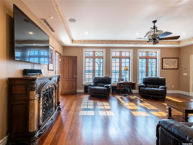 living room featuring a tray ceiling, ceiling fan, a fireplace, and dark wood-type flooring