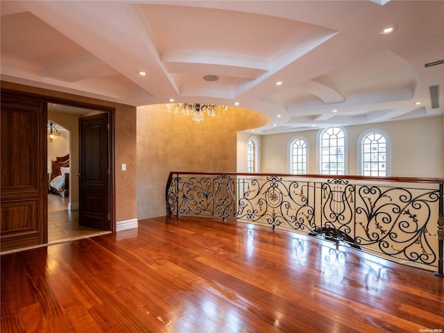 spare room featuring beamed ceiling, wood-type flooring, coffered ceiling, and an inviting chandelier