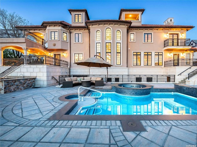 back house at dusk with an outdoor hangout area, a balcony, a patio, and a pool with hot tub