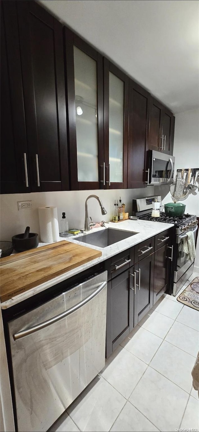 kitchen with light tile patterned floors, dark brown cabinetry, stainless steel appliances, and sink