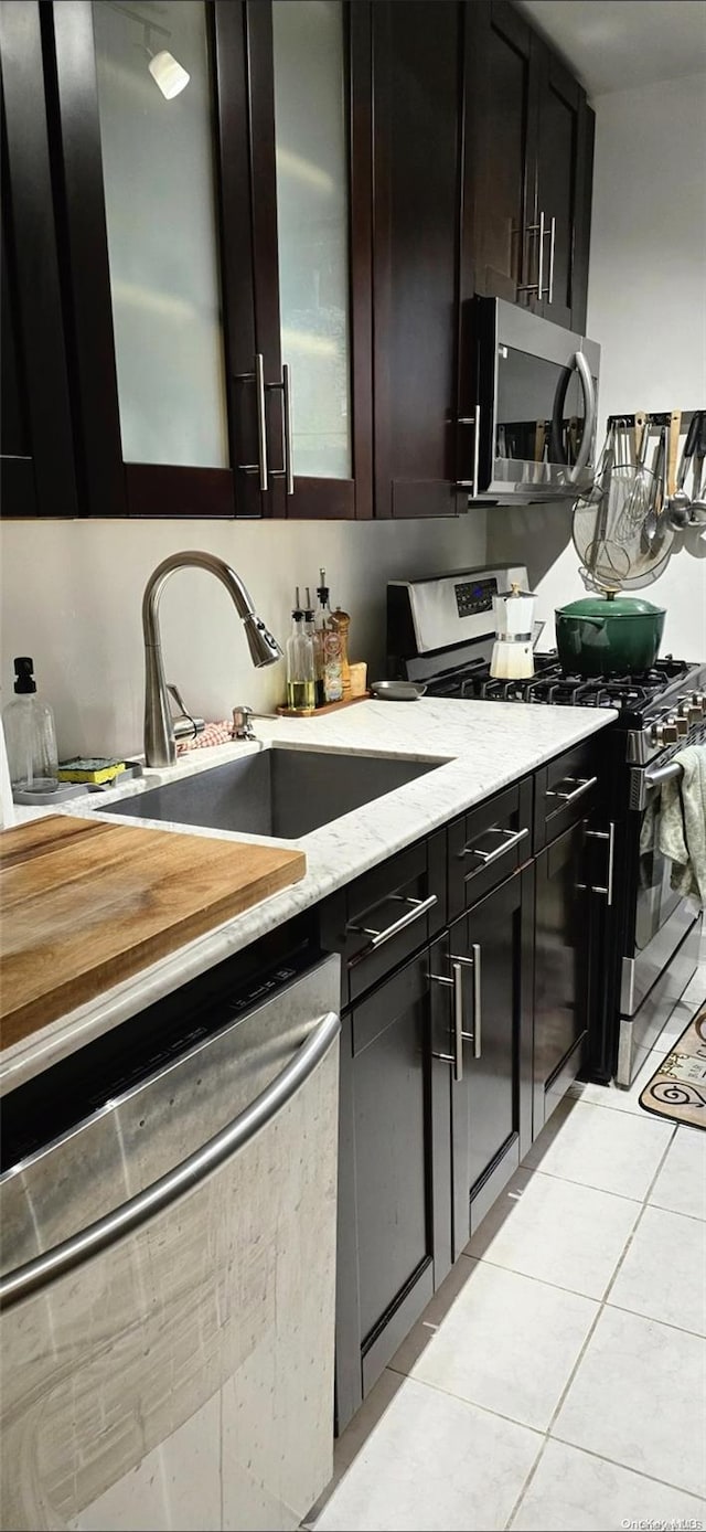 kitchen featuring sink, light tile patterned floors, light stone counters, dark brown cabinetry, and stainless steel appliances