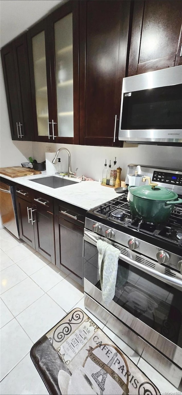 kitchen with light tile patterned flooring, dark brown cabinetry, stainless steel appliances, and sink