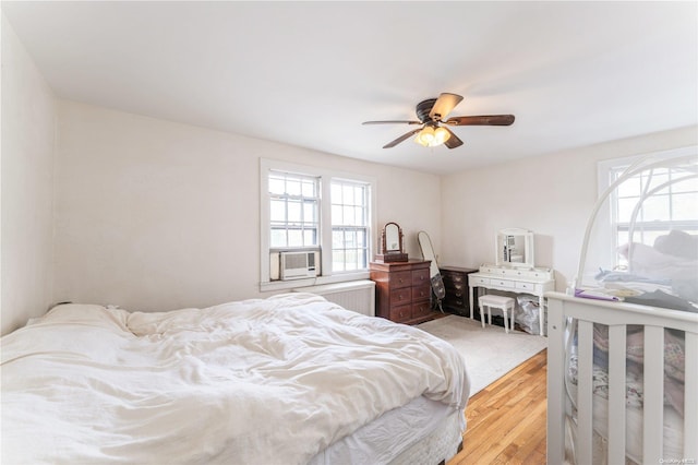 bedroom featuring radiator heating unit, light hardwood / wood-style floors, ceiling fan, and cooling unit