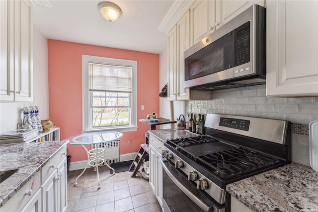 kitchen with light stone countertops, light tile patterned floors, tasteful backsplash, radiator heating unit, and stainless steel appliances