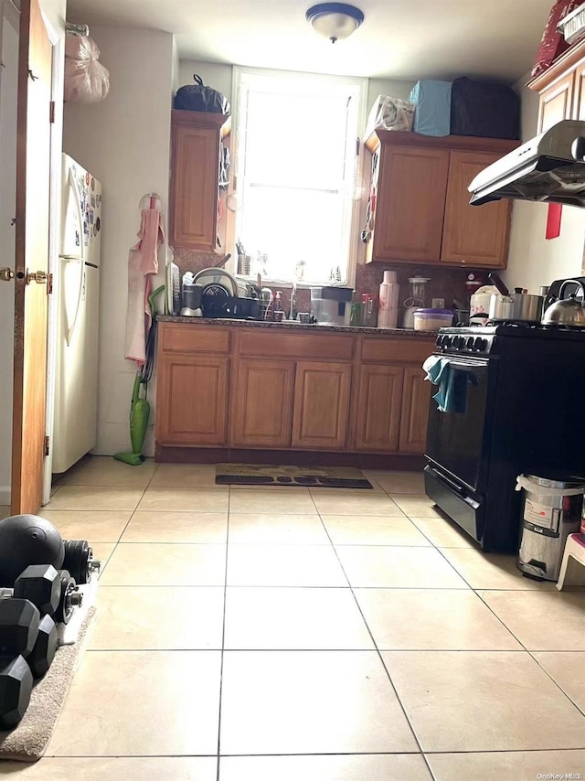 kitchen with white refrigerator, sink, black gas range oven, light tile patterned flooring, and extractor fan