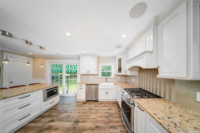 kitchen with stainless steel appliances, sink, wood-type flooring, white cabinets, and hanging light fixtures