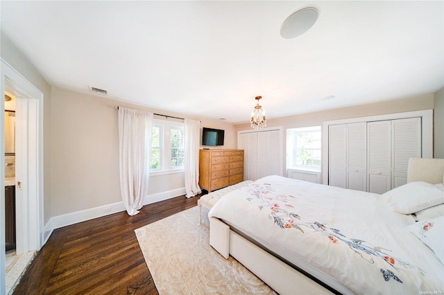 bedroom with dark hardwood / wood-style floors, two closets, a chandelier, and multiple windows