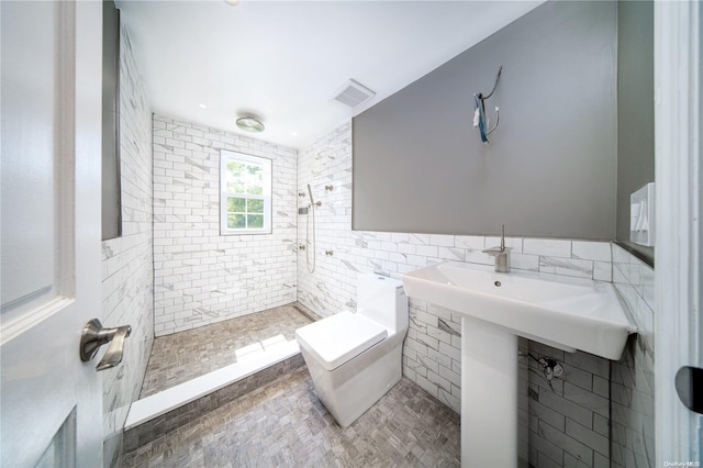 bathroom featuring a tile shower, toilet, and tile walls