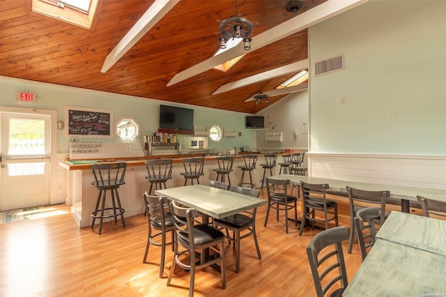 dining room featuring vaulted ceiling with skylight, light wood-type flooring, indoor bar, and wooden ceiling