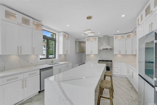 kitchen featuring a center island, white cabinets, wall chimney range hood, appliances with stainless steel finishes, and decorative light fixtures