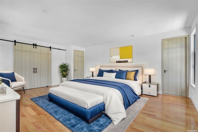 bedroom with a barn door and light hardwood / wood-style floors