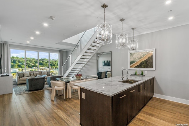 kitchen featuring pendant lighting, sink, light stone countertops, light hardwood / wood-style floors, and dark brown cabinetry