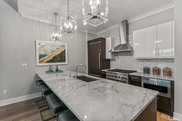 kitchen with dark brown cabinetry, sink, wall chimney range hood, built in appliances, and white cabinetry