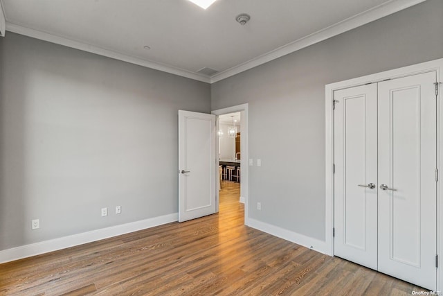 unfurnished bedroom with hardwood / wood-style floors, a closet, and ornamental molding