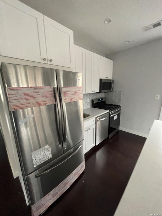 kitchen with white cabinets, appliances with stainless steel finishes, tasteful backsplash, and dark wood-type flooring