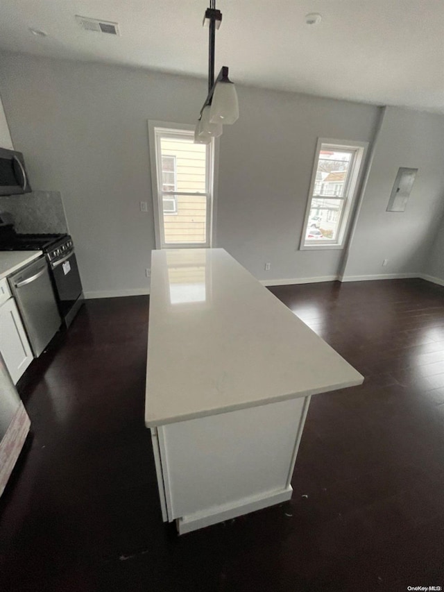 kitchen featuring appliances with stainless steel finishes, decorative light fixtures, white cabinets, dark hardwood / wood-style floors, and a kitchen island