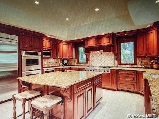 kitchen featuring stainless steel appliances, light stone counters, a breakfast bar, light tile patterned flooring, and a center island with sink