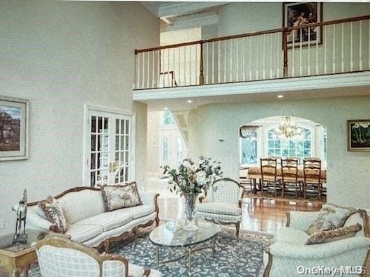 living room with french doors, a towering ceiling, hardwood / wood-style floors, and an inviting chandelier