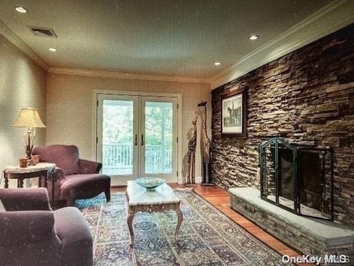 living room with hardwood / wood-style floors, a stone fireplace, ornamental molding, and french doors