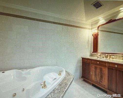 bathroom featuring tiled bath, vanity, tile walls, and ornamental molding