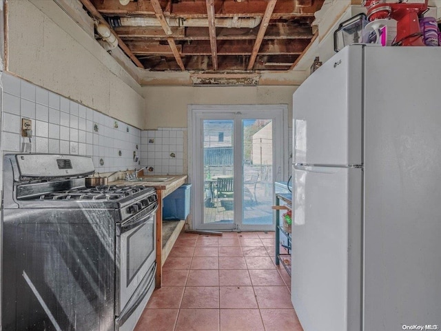 kitchen with sink, gas range, tile patterned flooring, tile walls, and white fridge