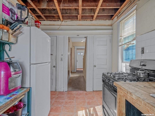 kitchen featuring light tile patterned flooring, white fridge, butcher block counters, and black range with gas cooktop