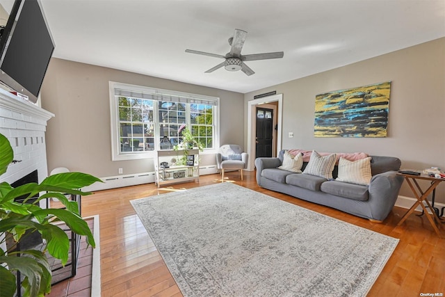 living room featuring baseboard heating, ceiling fan, a fireplace, and light wood-type flooring