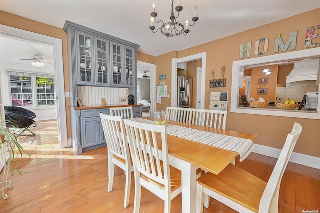 dining area with ceiling fan with notable chandelier and light hardwood / wood-style floors