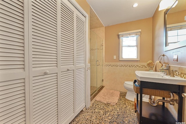 bathroom with vanity, toilet, a shower with shower door, and tile walls