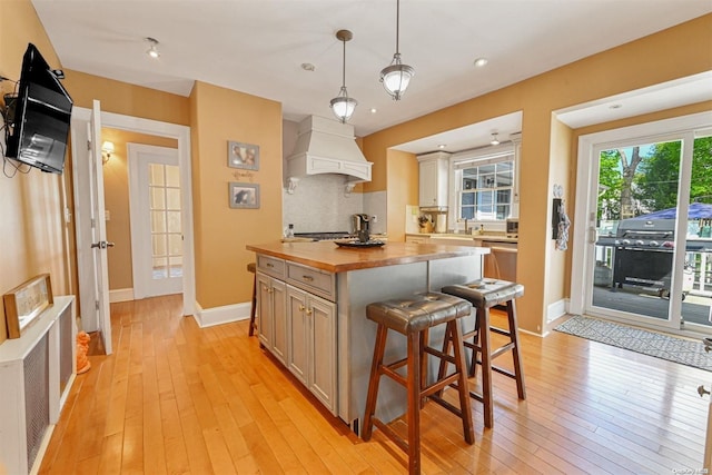 kitchen featuring pendant lighting, premium range hood, a kitchen island, light hardwood / wood-style floors, and butcher block counters