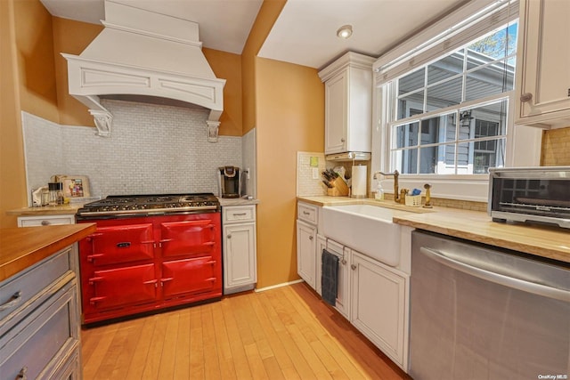 kitchen with sink, light hardwood / wood-style flooring, custom range hood, appliances with stainless steel finishes, and butcher block counters