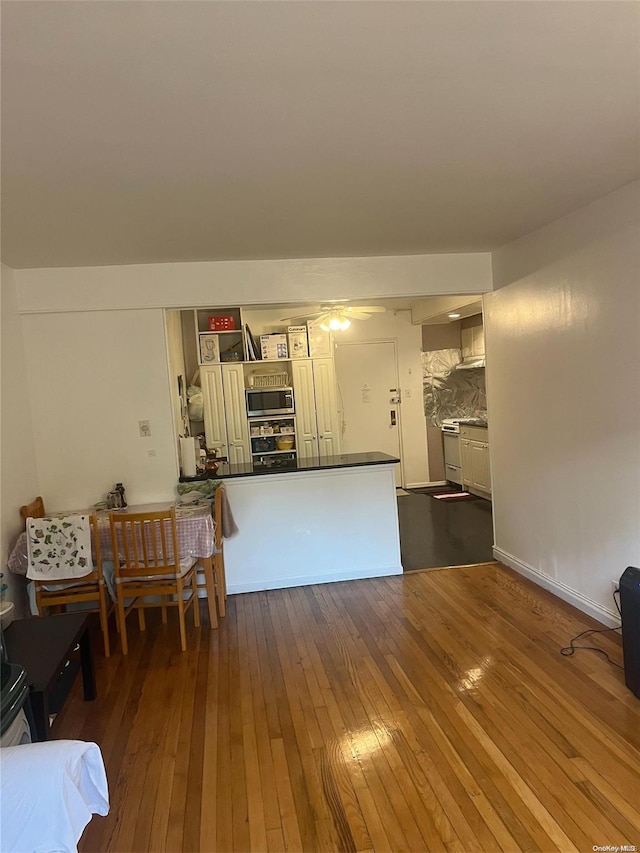 interior space featuring stainless steel microwave, dark wood-type flooring, tasteful backsplash, kitchen peninsula, and black oven