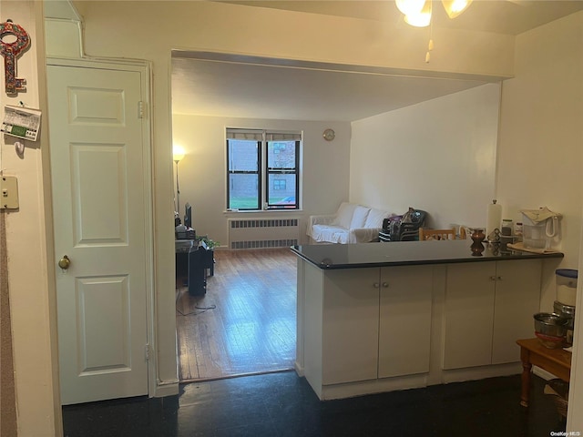 kitchen with kitchen peninsula, ceiling fan, radiator heating unit, dark hardwood / wood-style floors, and white cabinetry