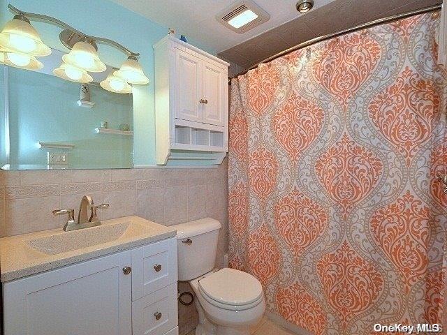 bathroom featuring vanity, toilet, and tile walls