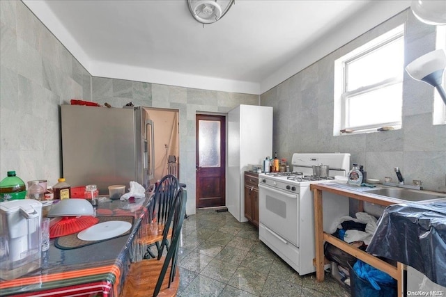 kitchen featuring stainless steel fridge, tile walls, white gas stove, and sink