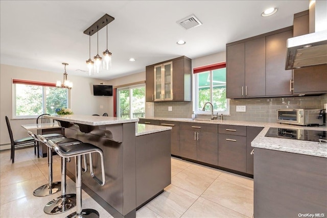 kitchen with light stone countertops, a center island, hanging light fixtures, a kitchen breakfast bar, and backsplash