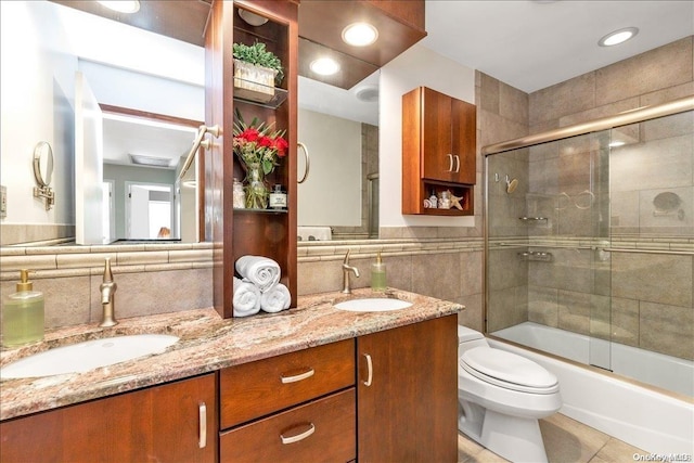 full bathroom with vanity, tile patterned floors, combined bath / shower with glass door, toilet, and tile walls