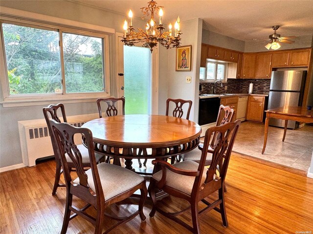 dining area with ceiling fan with notable chandelier, radiator heating unit, sink, and light hardwood / wood-style flooring