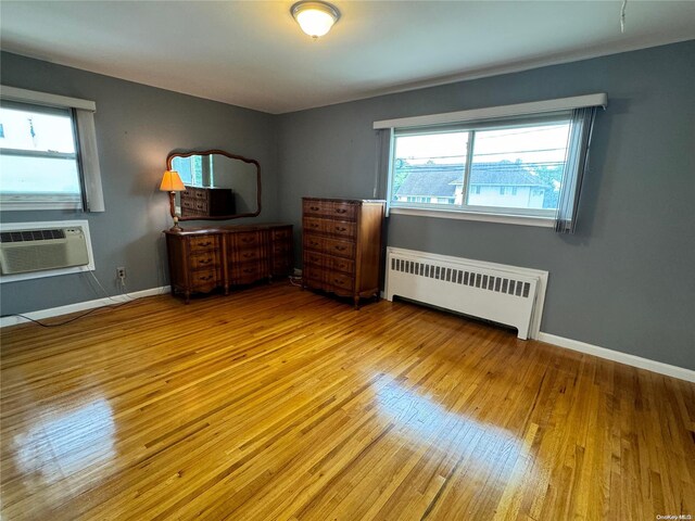 unfurnished bedroom with light hardwood / wood-style floors, a wall unit AC, and radiator