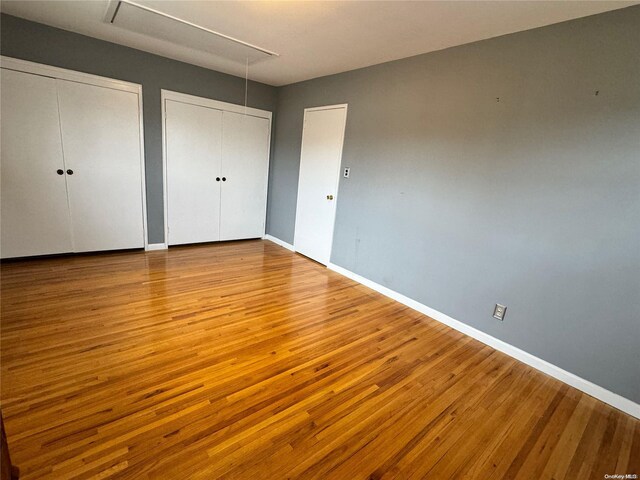 unfurnished bedroom with light hardwood / wood-style flooring and two closets