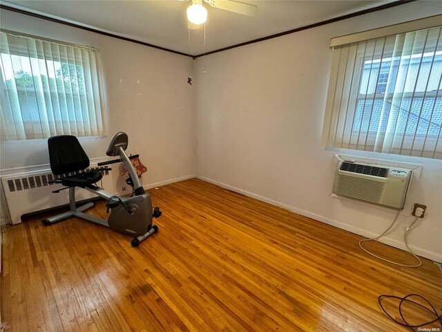 exercise area featuring radiator, ceiling fan, wood-type flooring, and a wall mounted air conditioner