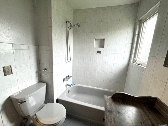 bathroom featuring tiled shower / bath combo, toilet, and tile walls