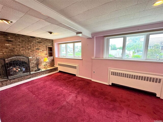 unfurnished living room with radiator heating unit, a healthy amount of sunlight, and a brick fireplace