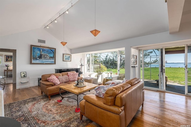 living room with a water view, rail lighting, high vaulted ceiling, and light wood-type flooring