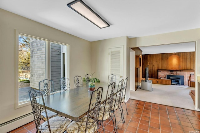 dining space with a wood stove, wood walls, carpet floors, and a baseboard heating unit