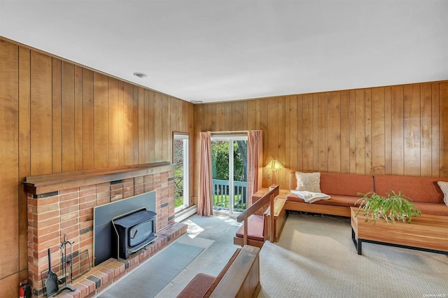 living room with a wood stove, wooden walls, carpet floors, and a baseboard heating unit