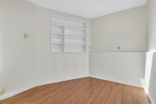 spare room featuring built in shelves and light wood-type flooring