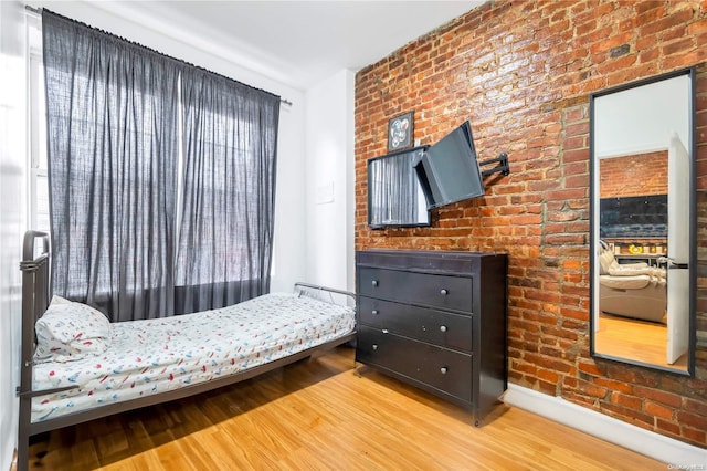 bedroom with hardwood / wood-style floors and brick wall