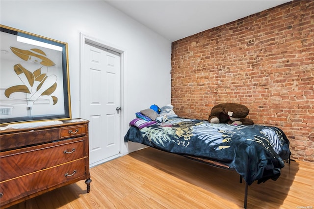 bedroom featuring light hardwood / wood-style flooring and brick wall